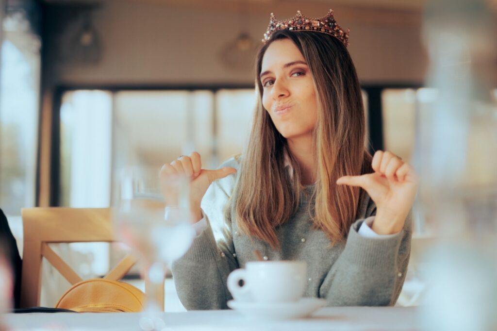 A smug woman pointing to herself while wearing a crown.