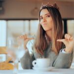 A smug woman pointing to herself while wearing a crown.