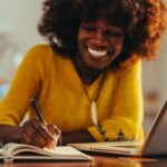 Selective focus on the businesswoman's hand, writing down tasks and notes in an agenda while working remotely from home. A happy interracial female entrepreneur is taking notes in the agenda.