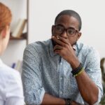 A man sits across from a woman, looking thoughtful.