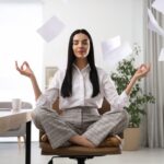 A woman meditates on a desk chair. Papers fly around her.