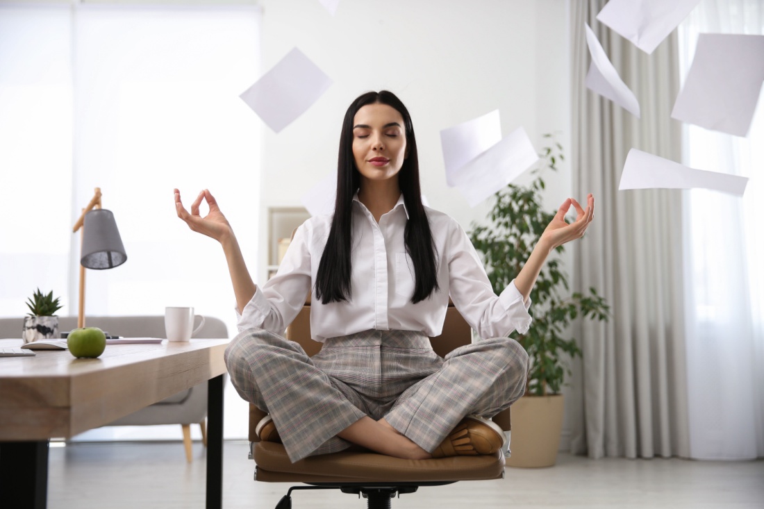 A woman meditates on a desk chair. Papers fly around her.