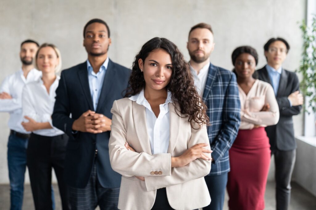 A woman stands in front of a group of people. All are professionally dressed.