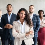 A woman stands in front of a group of people. All are professionally dressed.