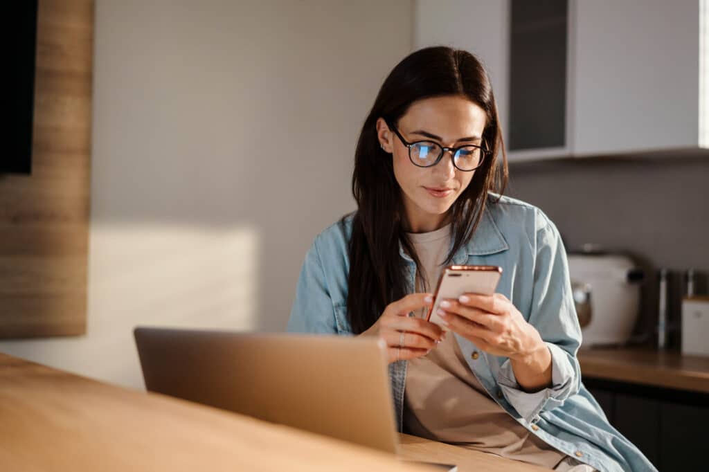 woman sitting at her desk while using her phone