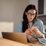 woman sitting at her desk while using her phone