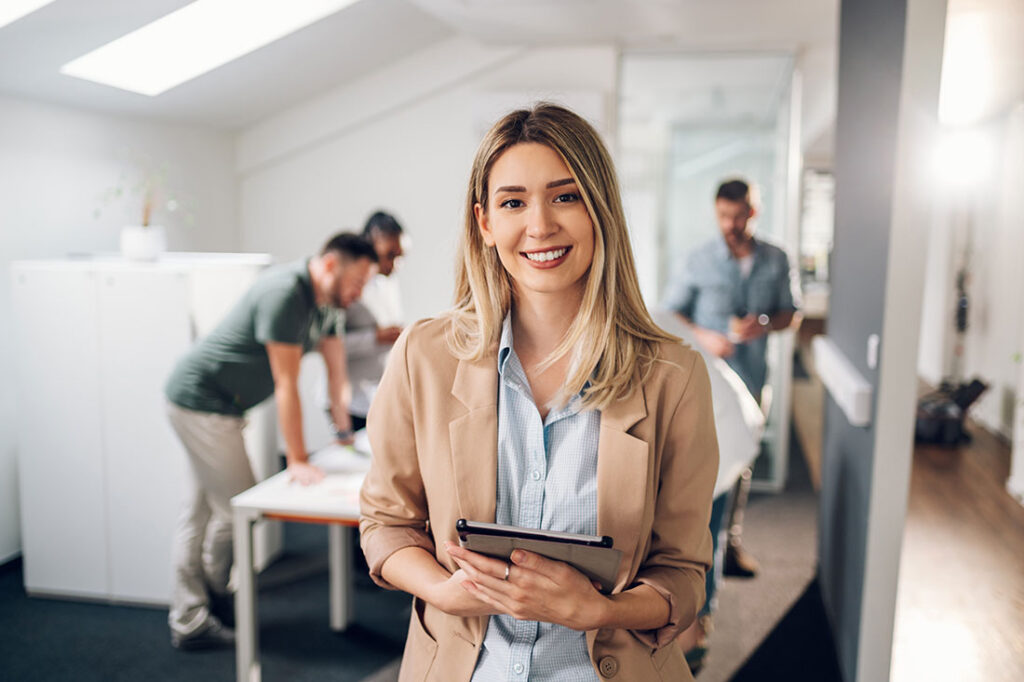 Smiling confident business leader looking at camera and standing in an office at team meeting