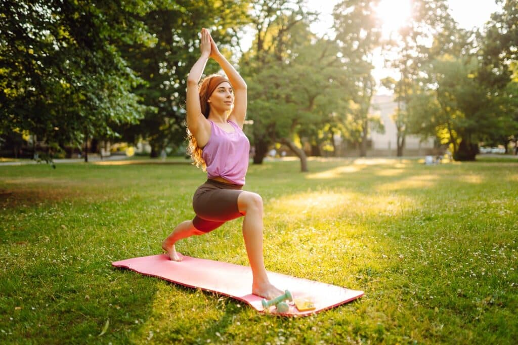 woman doing a yoga pose on a yoga mat in a park