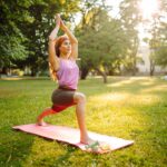 woman doing a yoga pose on a yoga mat in a park