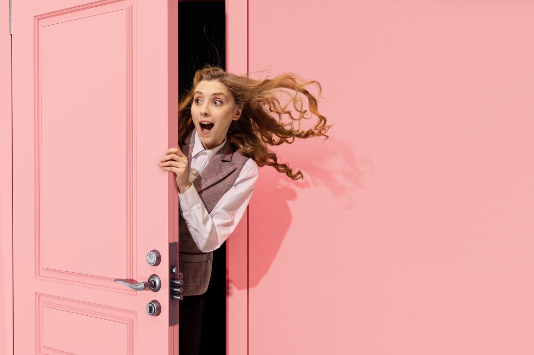 A woman peeks out from behind a pink door. a