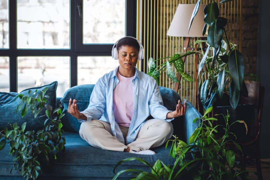 A woman meditates on her couch with headphones on.