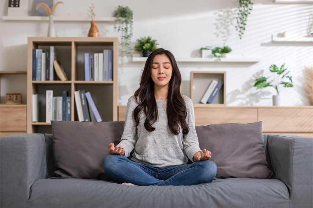 young woman doing yoga lotus pose to meditation and relax on couch during work