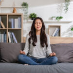 young woman doing yoga lotus pose to meditation and relax on couch during work