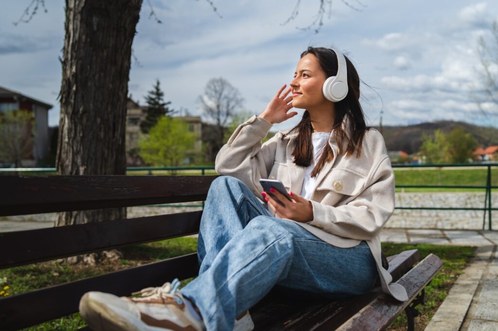 a woman sitting on a park bench wearing headphones and holding a phone in her hand.