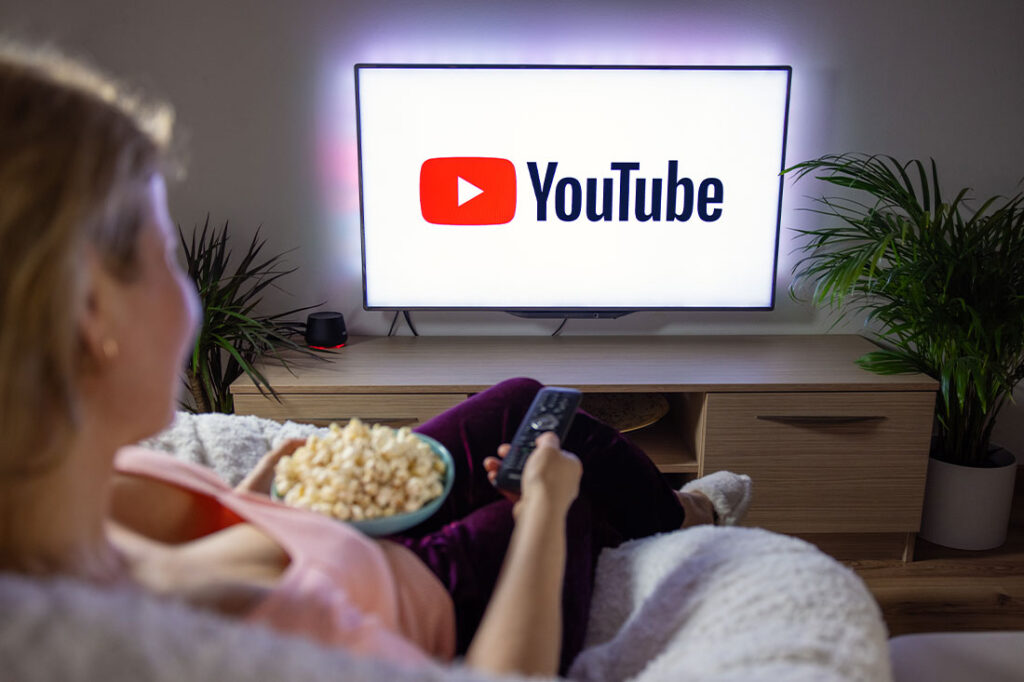 Woman holding popcorn and watching TV at home with YouTube logo on the screen.