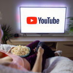 Woman holding popcorn and watching TV at home with YouTube logo on the screen.