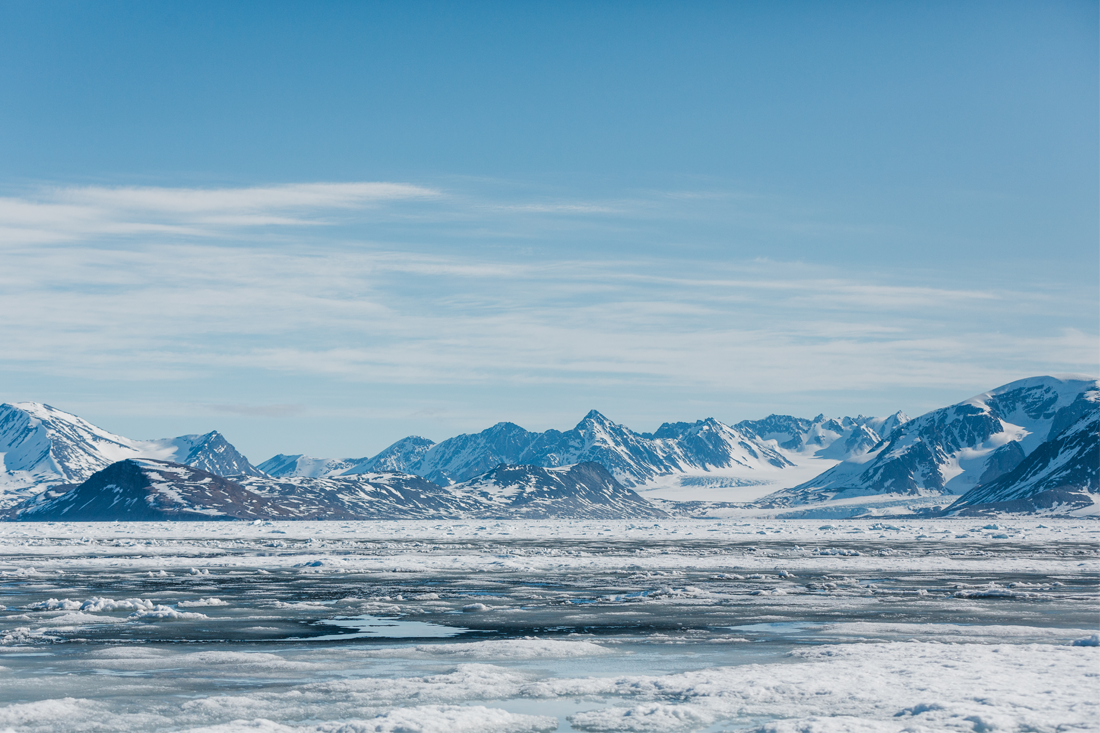 A landscape view of the Arctic, covered in ice, with mountains in the background.