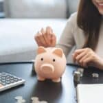 Close up shot of a woman's hands putting money in a piggy bank.