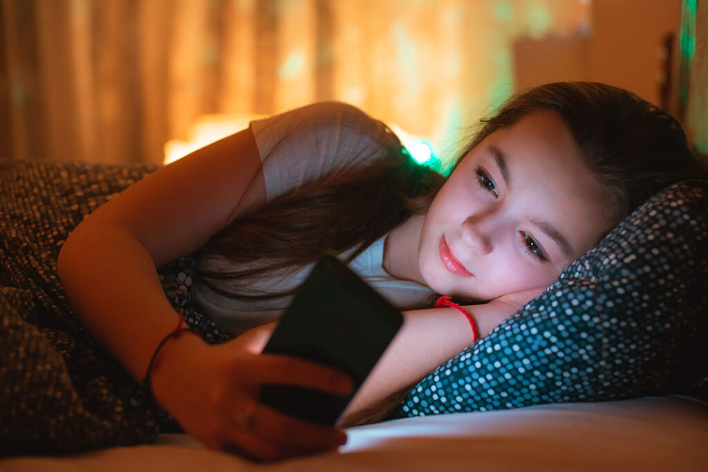 teen girl lying in bed at night and using smartphone