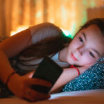 teen girl lying in bed at night and using smartphone