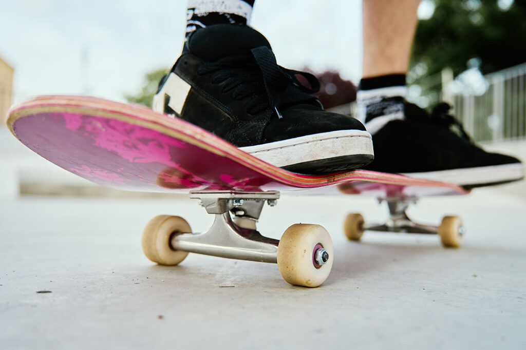 A close-up shot of a skateboarder's feet on a pink skateboard at a skate park