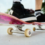 A close-up shot of a skateboarder's feet on a pink skateboard at a skate park