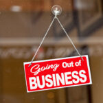 Red sign hanging at the glass door of a shop saying: "Going out of business".